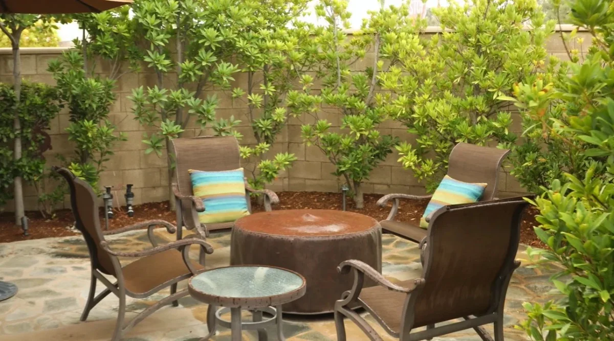 Outdoor fire pit table surrounded by patio seating and mature landscaping